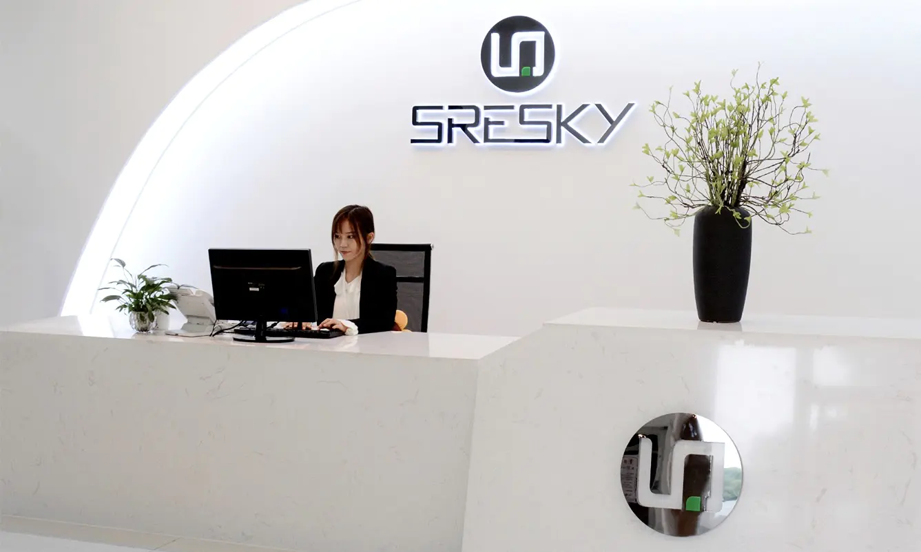 showing a modern reception area at the SreSky factory A woman in professional attire sits behind a sleek white marble desk working on a computer
