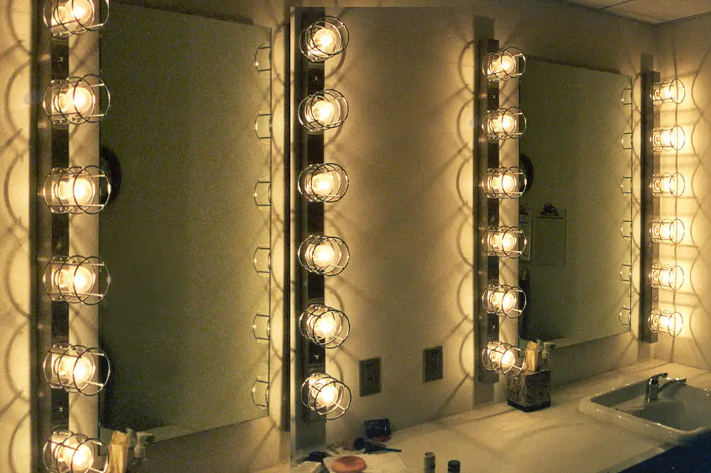 Kamar mandi yang cukup terang dengan cermin di dinding menampilkan perlengkapan lampu ruang ganti