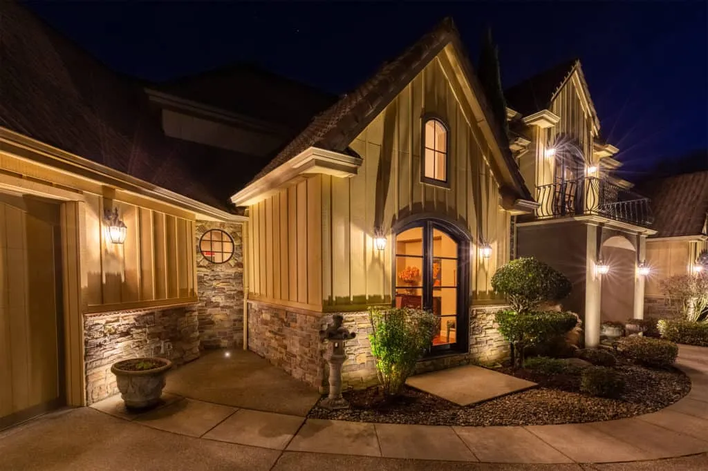 Una casa elegante de noche iluminada por luces exteriores bien colocadas que resaltan los detalles arquitectónicos y paisajísticos.