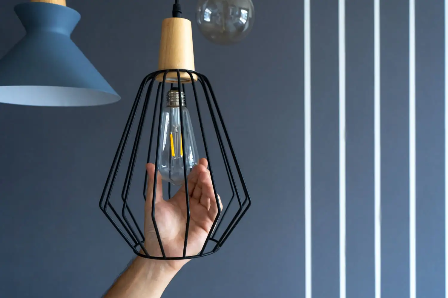 Hand holding light bulb in cage hanging from wall Image for How to Change a Light Fixture guide