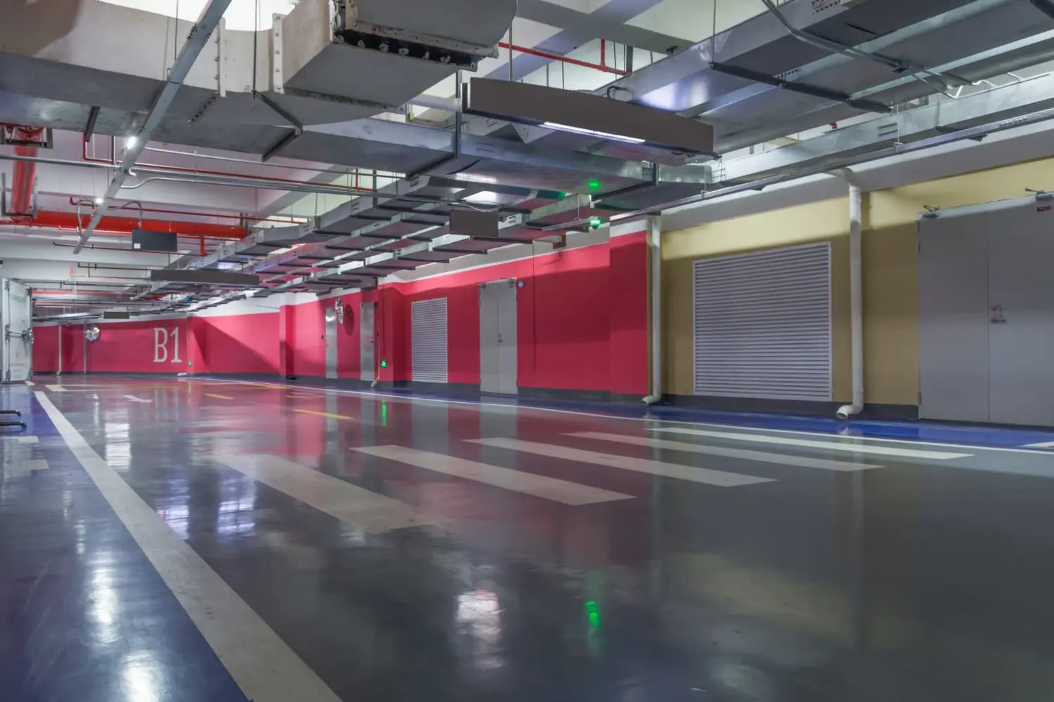 Spacious parking garage with red walls and blue lights illuminated by top parking lot lighting fixtures